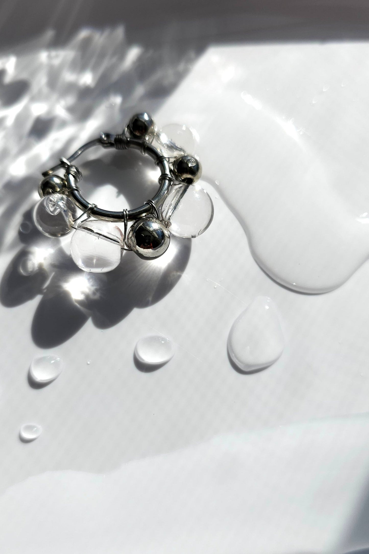 GINRO earring with hand-molded clear orb and silver orb, inspired by frozen dew shimmering in light, shown on neutral background.
