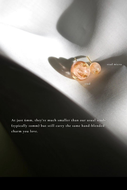 A 10mm orb stud in orange beige tone, HARU stud, compared with a 6mm orb stud in orange beige tone, HARU micro stud on a flat surface