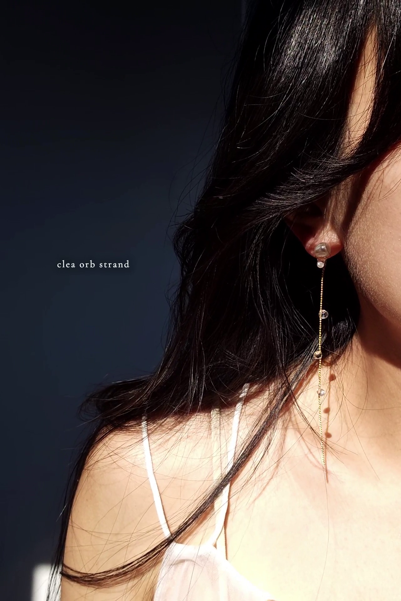 Close-up of a person wearing a HISEN aqua drop earring with a clear orb strand attached