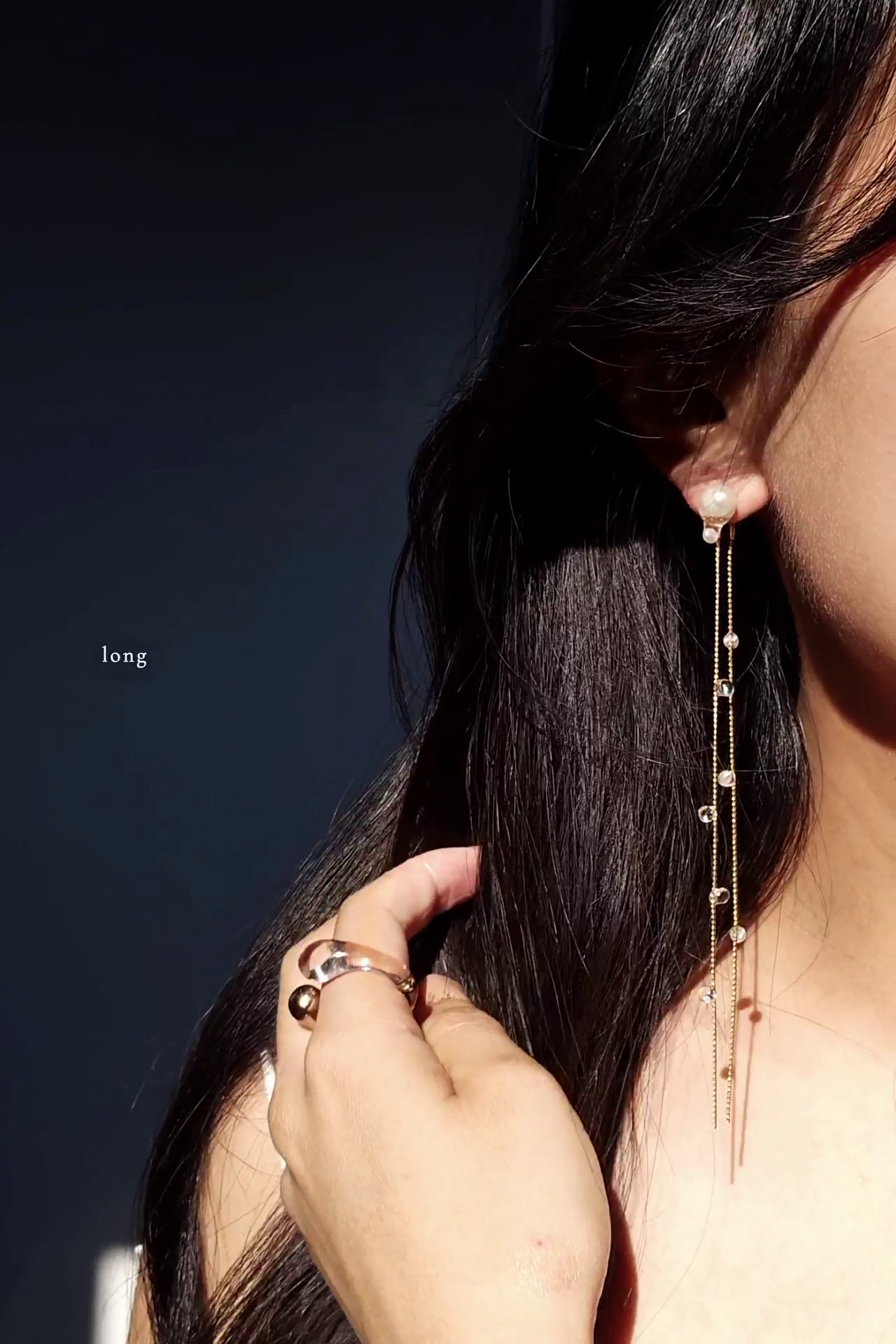 Close-up of a person wearing a delicate chain earring, HISEN aqua, long version with a dark background