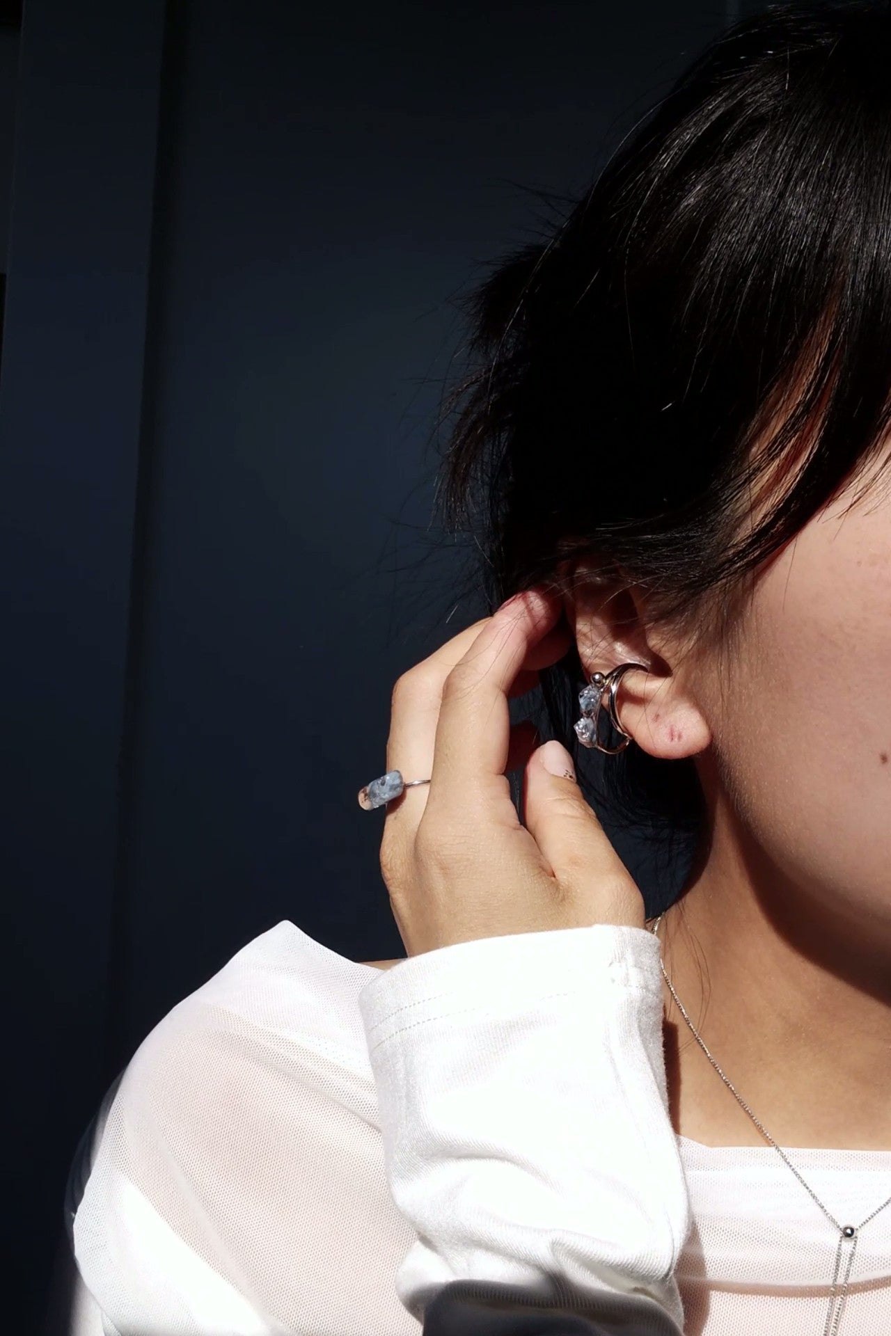 Close-up of a person wearing NAMI silver teardrop ear cuff, layered with soft silvery blue-gray tones.