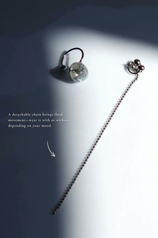 Flatlay of NAMI multiway ear cuff with dual-tone gray stone and removable chain, designed to evoke wave-like fluidity.