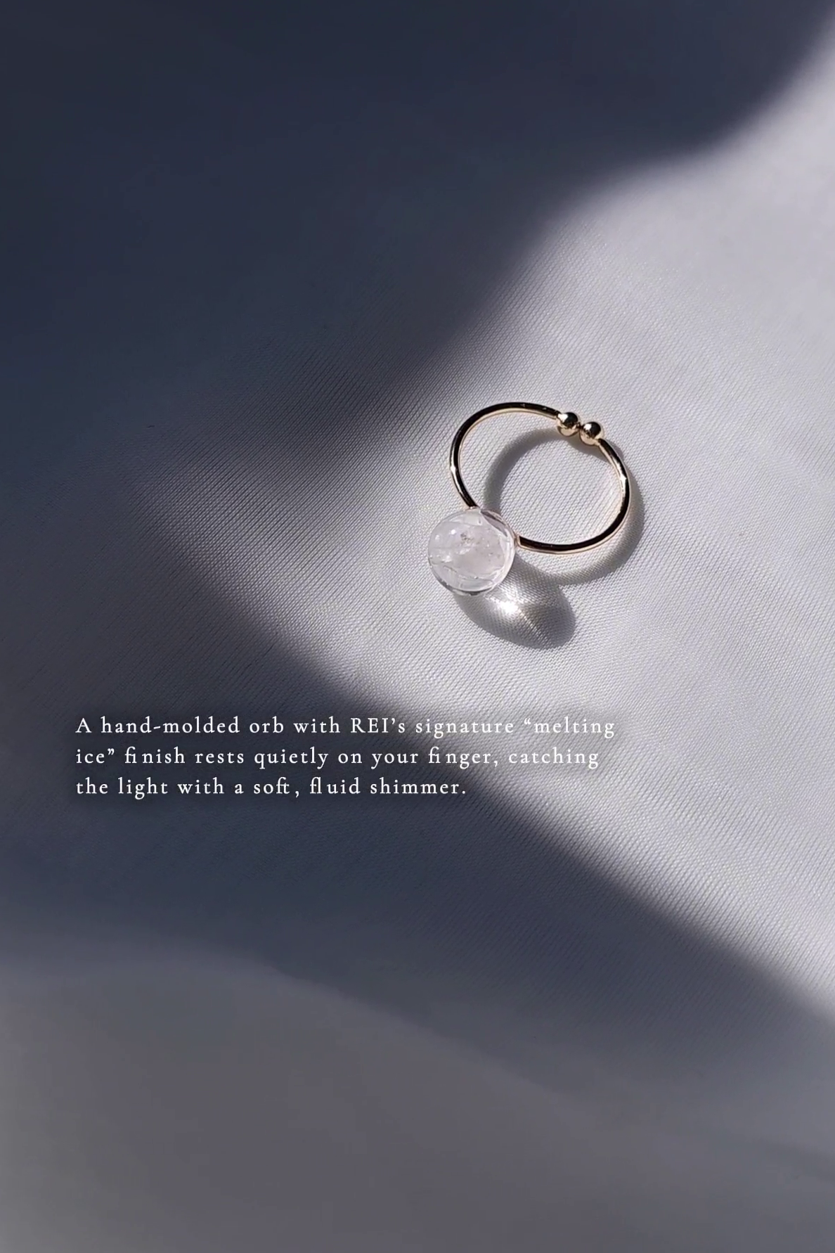 REI gold ring with hand-molded orb on a soft gray background