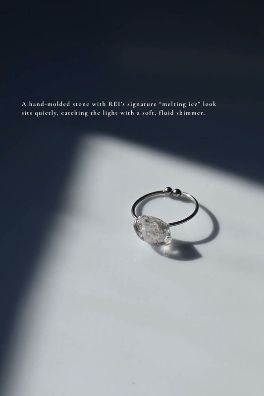 REI ring laid flat, showing its delicate metal band and hand-molded centerpiece resembling melting ice.