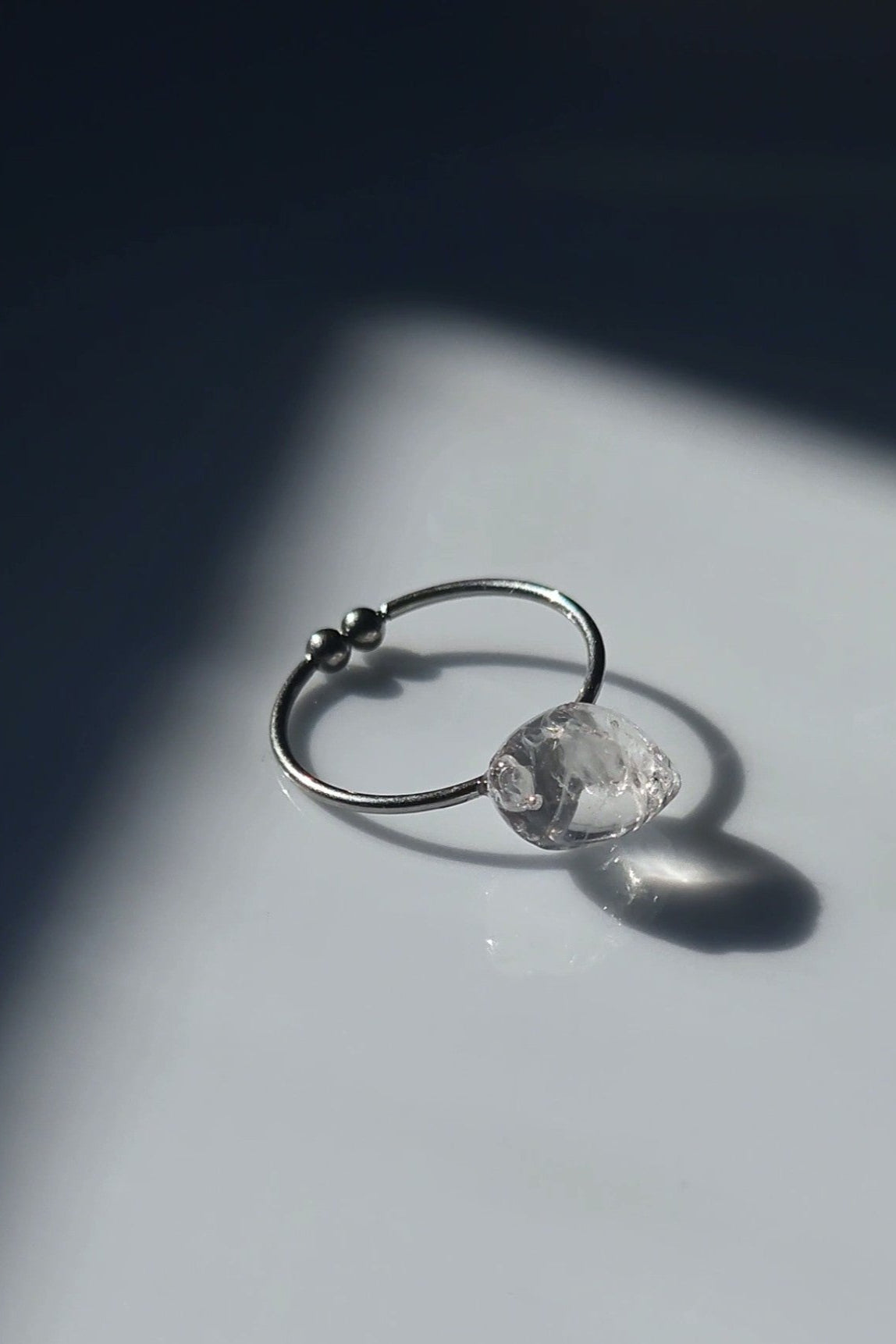 REI ring laid flat, showing its delicate metal band and hand-molded centerpiece resembling melting ice.