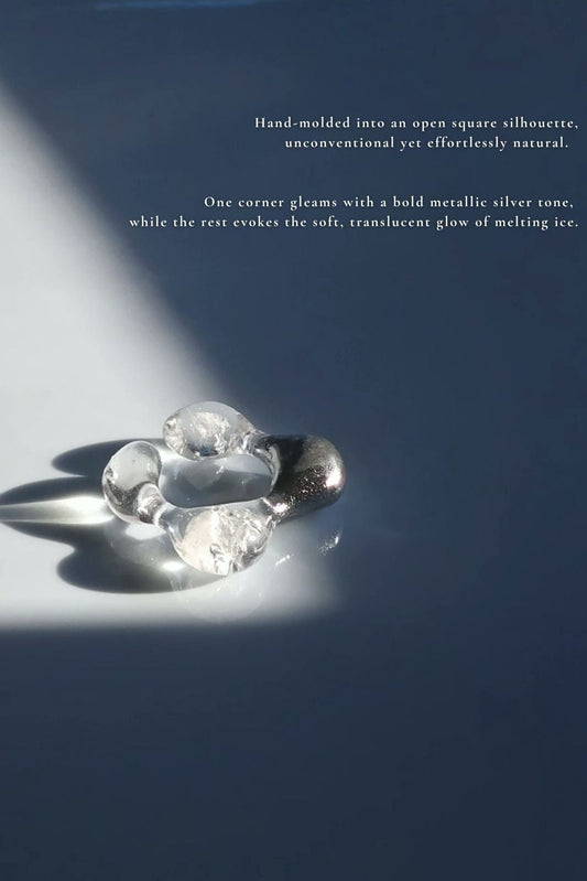 REI square ring laid flat, showing its open square silhouette with one metallic silver corner and translucent, ice-like finish.