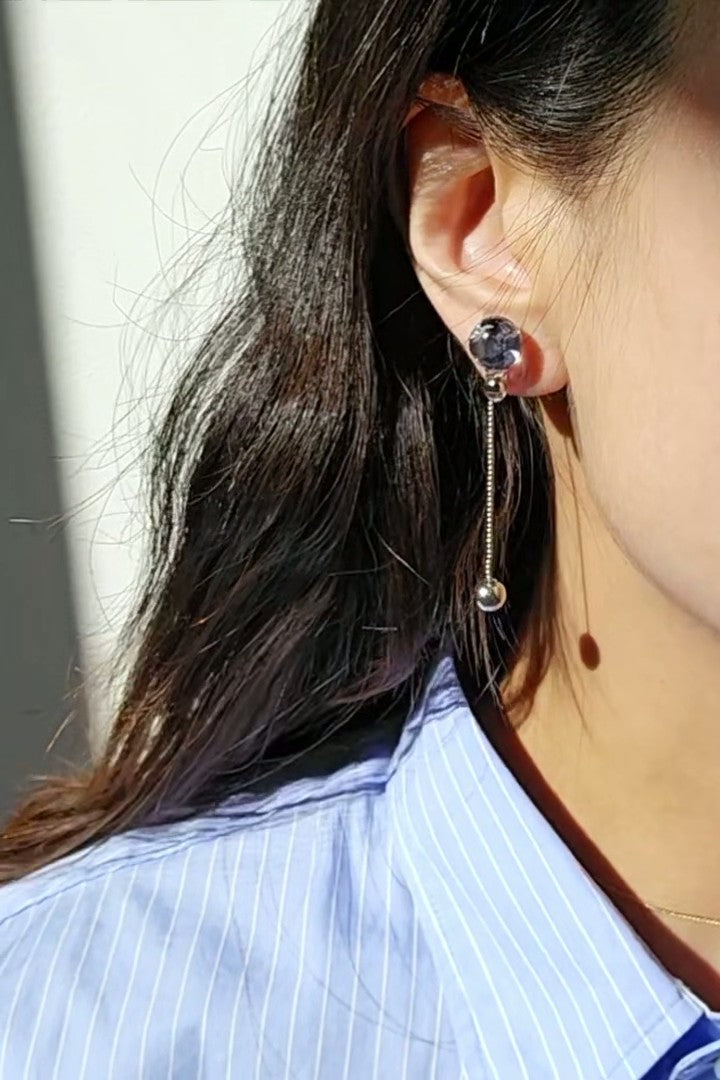 Model wearing SORA short drop earring with shimmering chain and hand-blended blue orb that changes color with the light.
