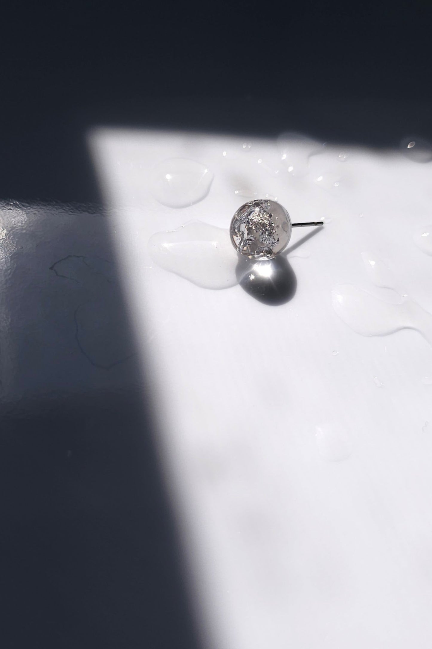 a close up of the SUIKO stud earring inspired by shimmering water reflections, minimalist and captivating in soft silver and luminous clear tones.