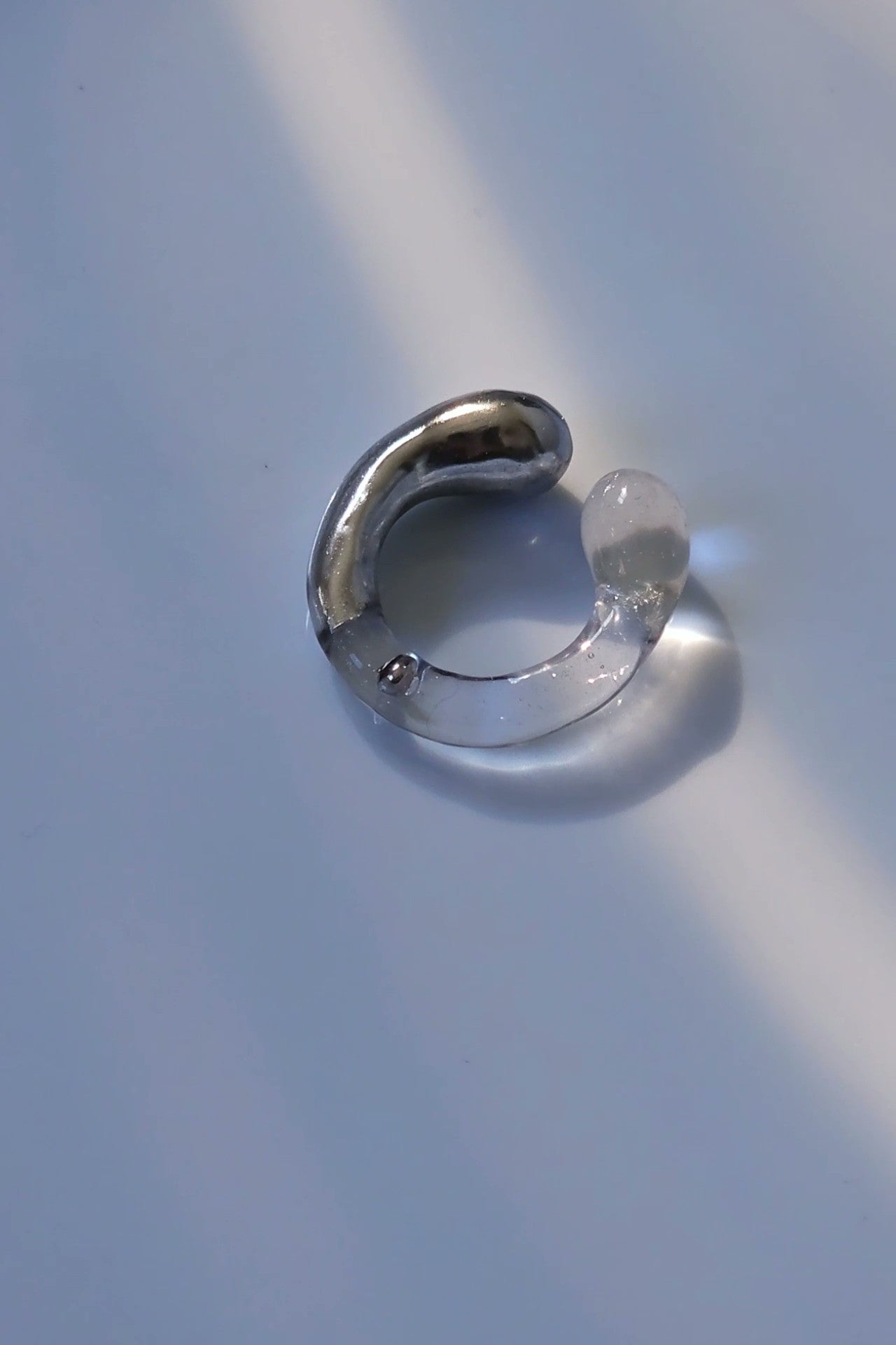 TORORI silver multiway ring with sculptural clear design, inspired by dripping water, shown laid on neutral background.