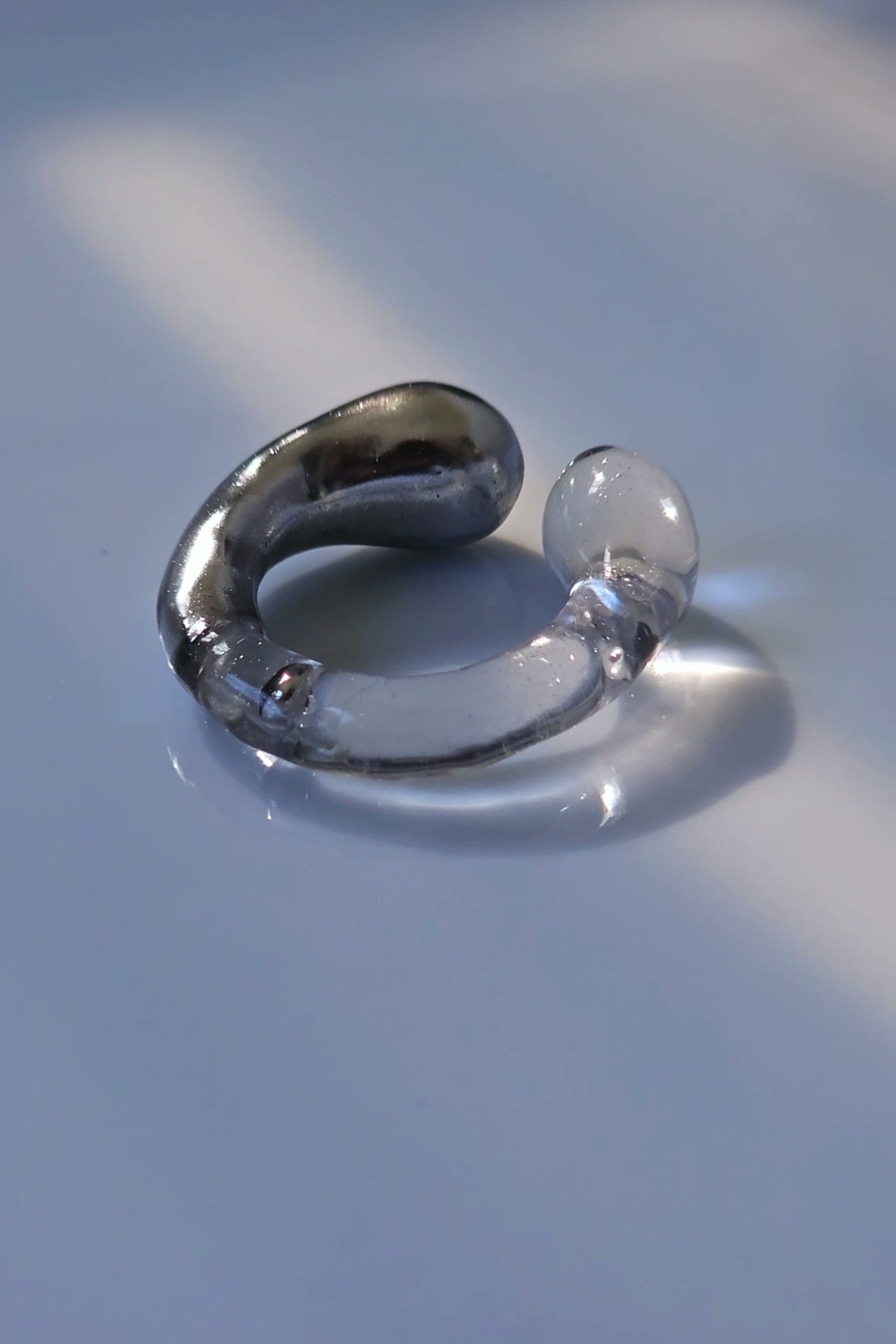 Close-up of TORORI silver multiway ring and ear cuff showing sculptural curves and clear resin accents inspired by water.
