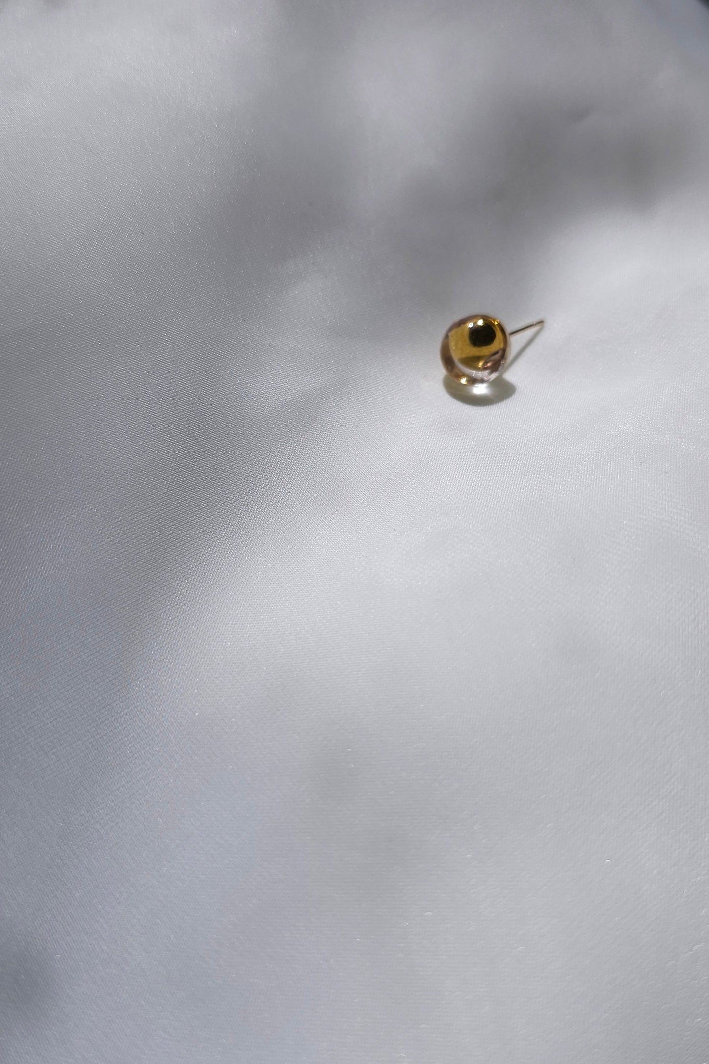zoom out image of the TSUYU gold stud earring, inspired by shimmering beads of dew, with warm golden reflections that change in the light.