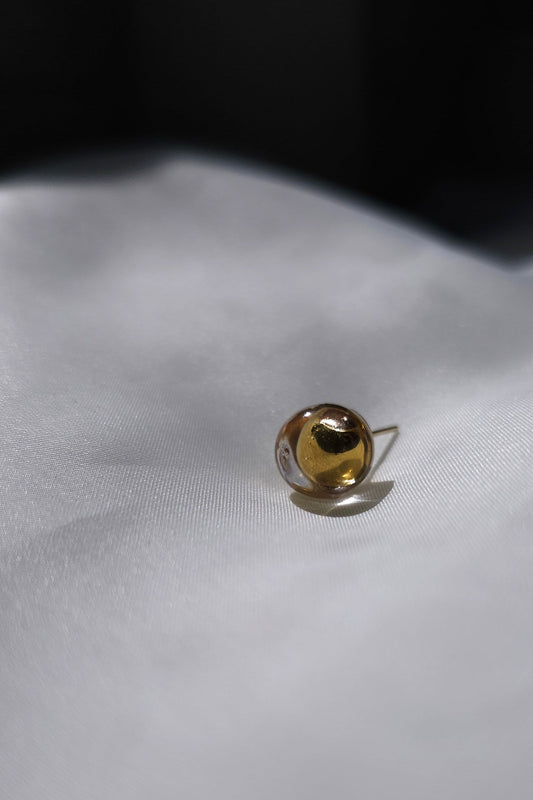 A close-up of TSUYU gold stud earring, inspired by shimmering beads of dew, with warm golden reflections that change in the light.