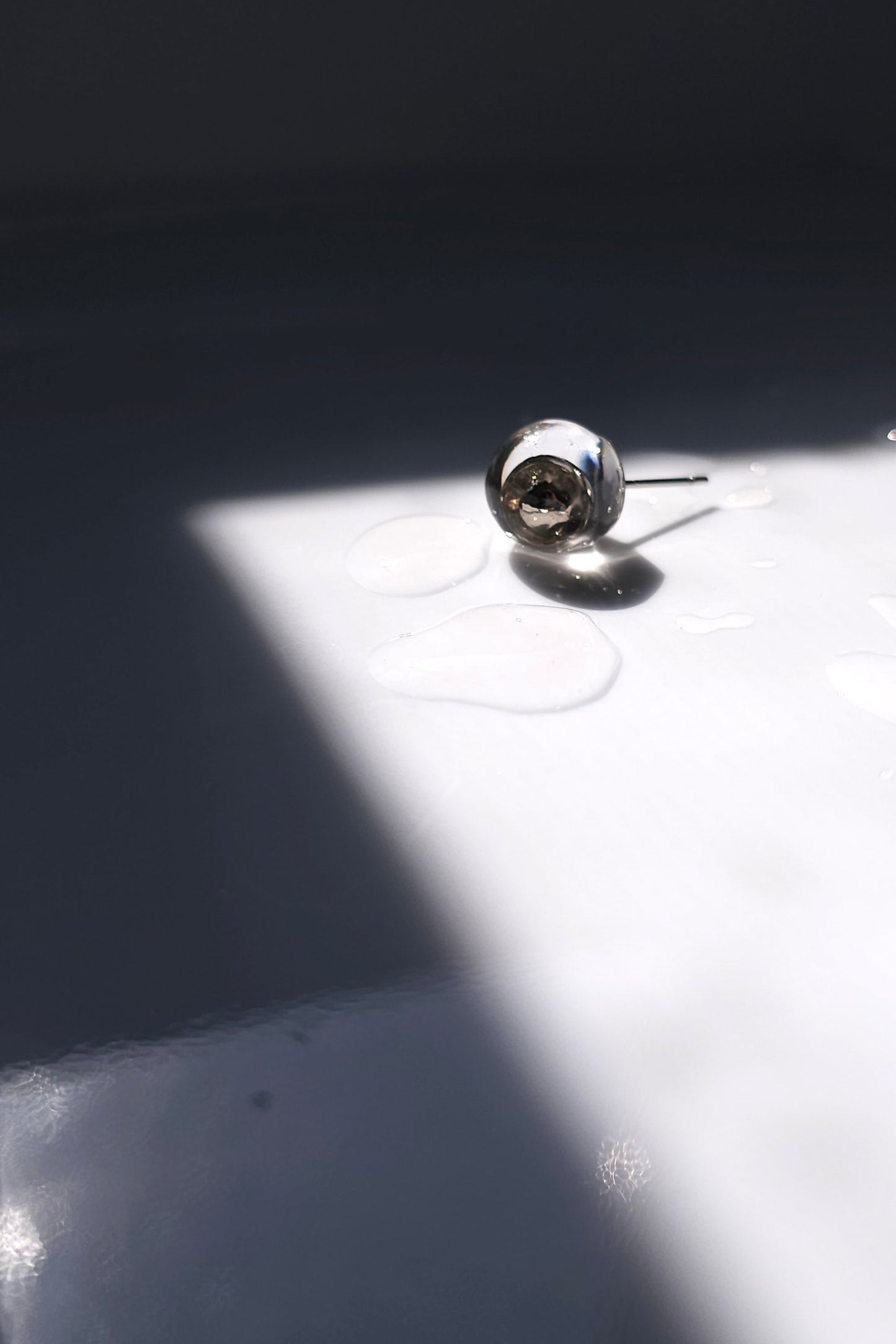 TSUYU silver stud earring, inspired by morning dew, with reflective clear and silver tones that shift with light.