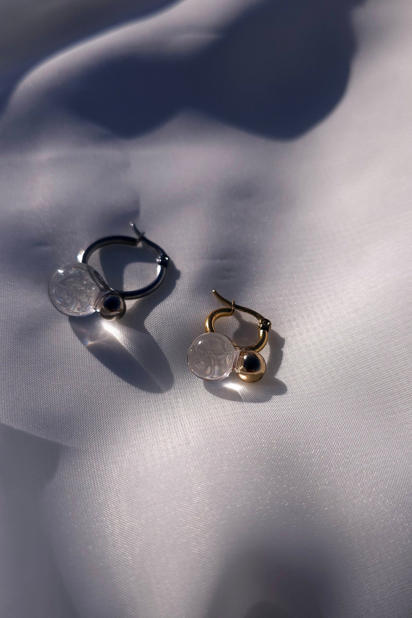 YOTSUYU gold earrings laid next to YOTSUYU silver with clear orb, handcrafted to echo night dew with a soft golden shimmer and airy elegance.