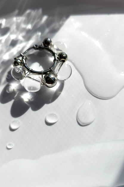 GINRO earring with hand-molded clear orb and silver orb, inspired by frozen dew shimmering in light, shown on neutral background. 