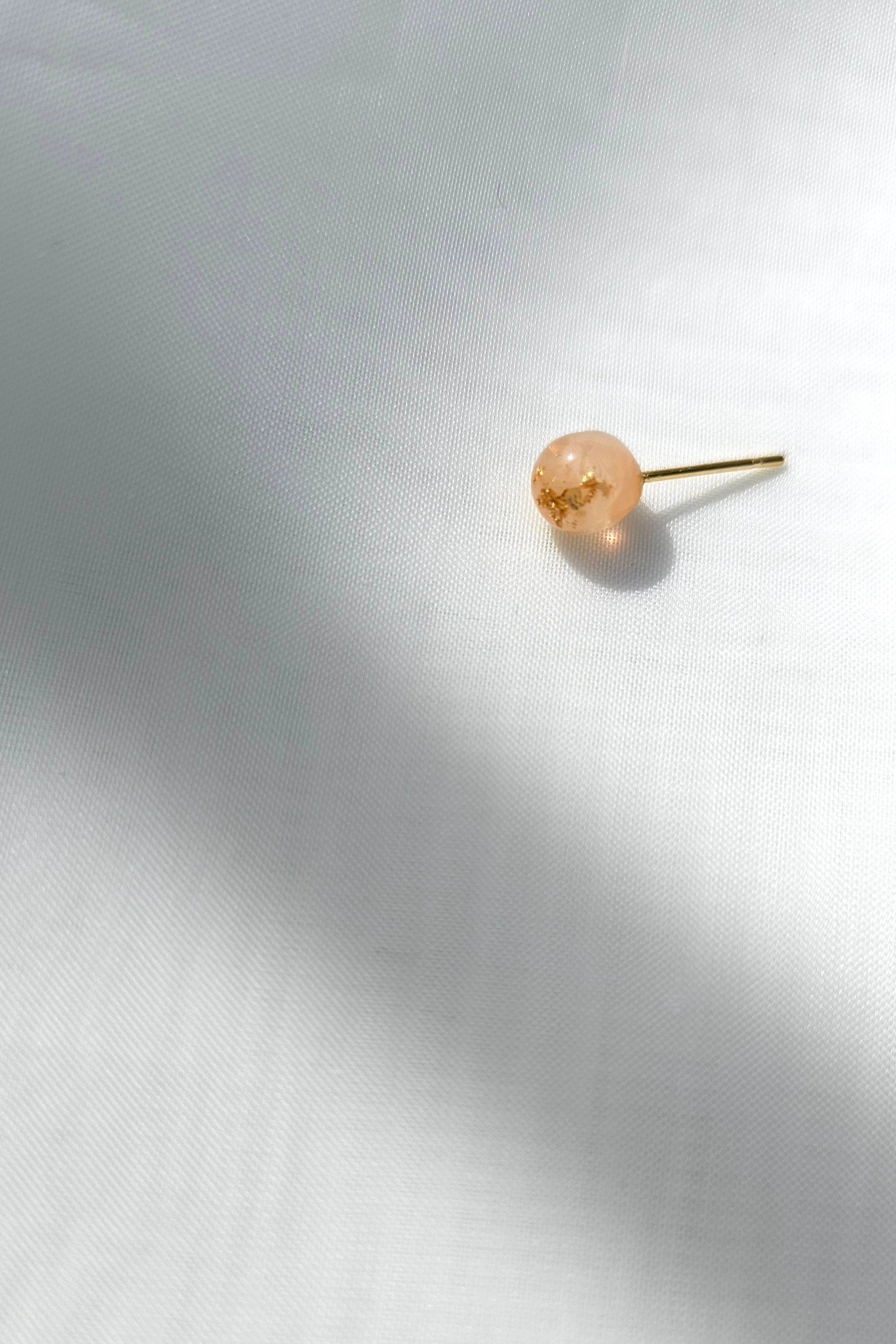 A single 6mm orb stud in orange beige tone, HARU micro stud, on a flat surface