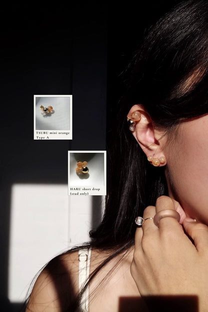 Close-up of a person wearing TSUBU mini orange orb earcuff on the helix with the stud from HARU orange series