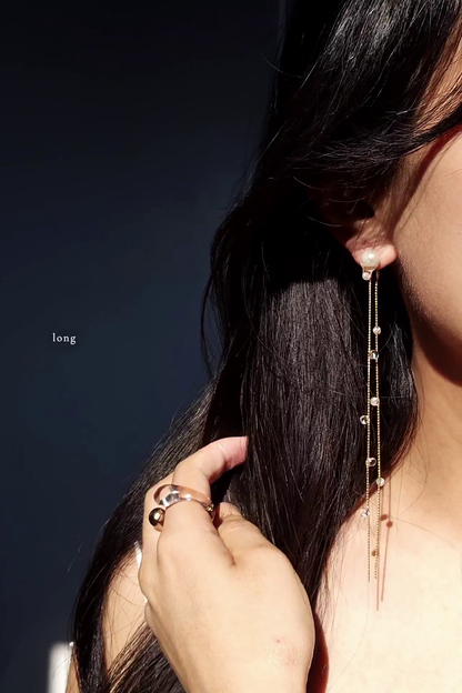 Close-up of a person wearing a delicate  chain earring, HISEN aqua, long version with a dark background