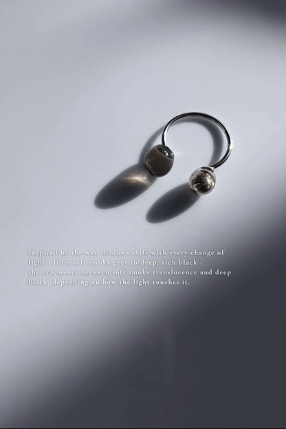 Double orb ring in translucent black and silver on flat surface