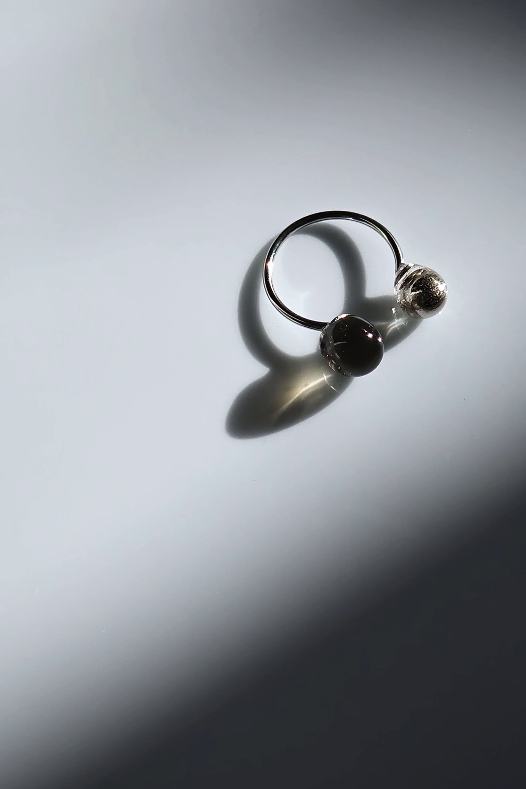 Double orb ring in translucent black and silver on flat surface showing deep black color.