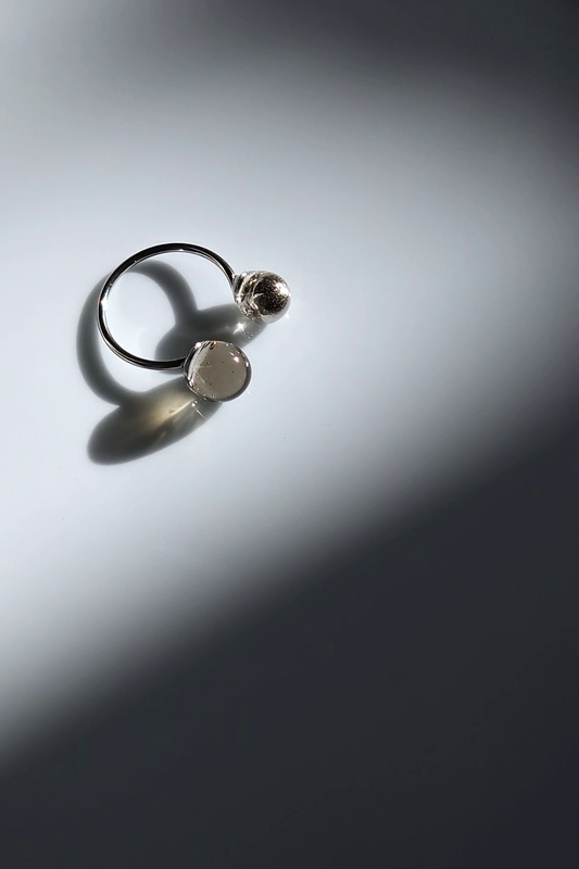 Double orb ring in translucent black and silver, KAGE ring on a flat surface.