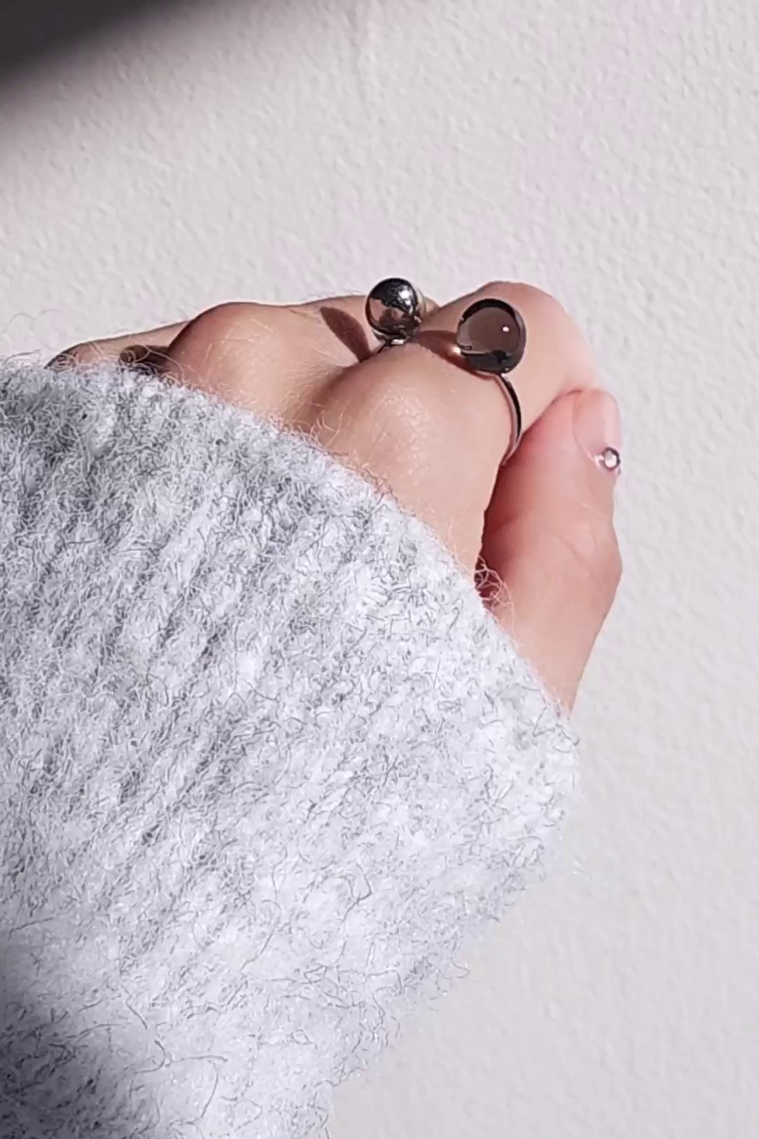 Double orb ring in translucent black and silver on index finger.