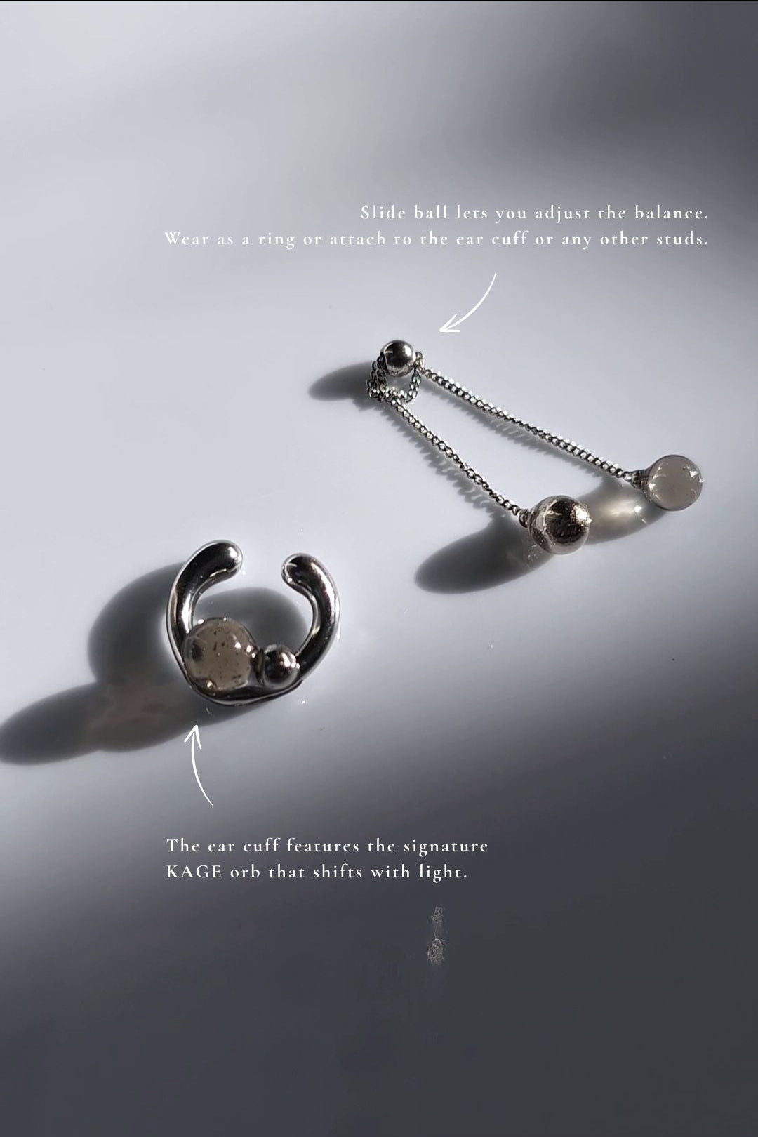 silver ear cuff with trancelucent black orb with detachable chain drop, KAGE ear cuff & ring, on a flat surface.