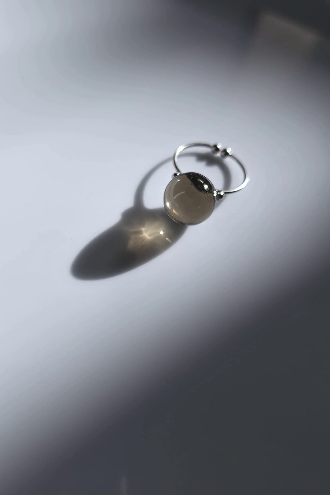 Silver ring with 12 mm translucent black orb, KAGE ring on flat surface.