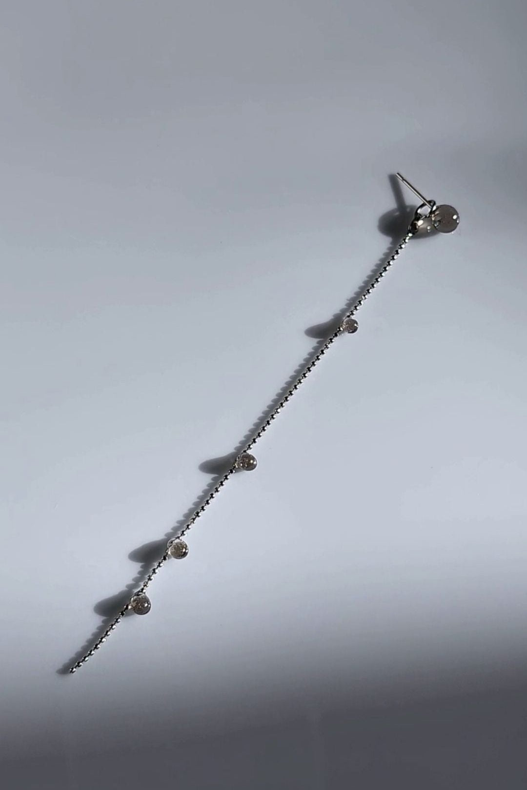 Delicate chain drop with translucent black orbs, KAGE silver chain drop on a flat surface.