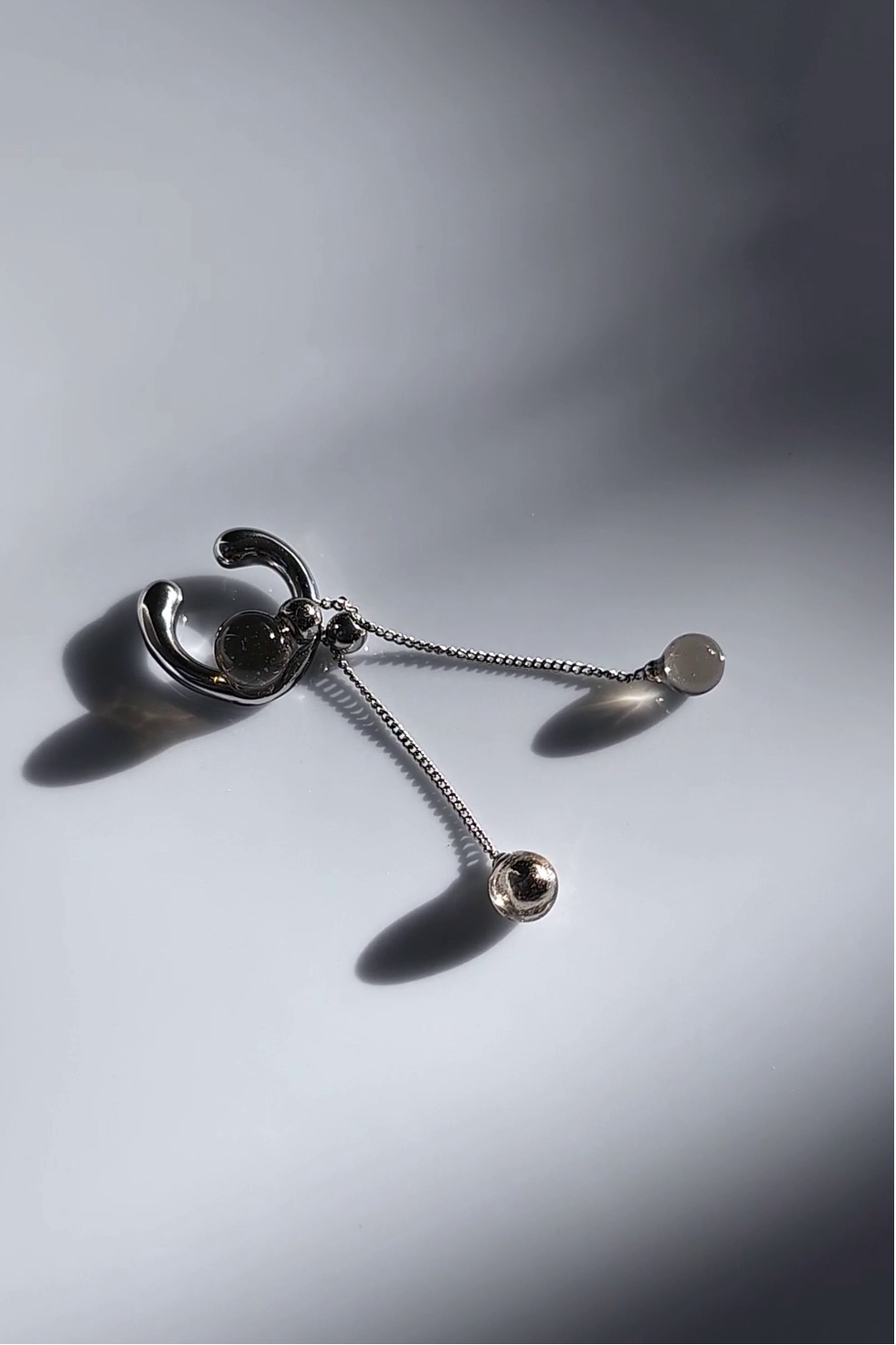 silver ear cuff with trancelucent black orb with detachable drop on flat surface.