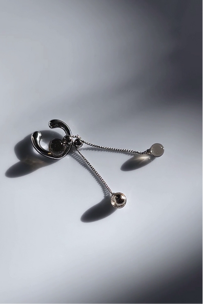 silver ear cuff with trancelucent black orb with detachable drop on flat surface.