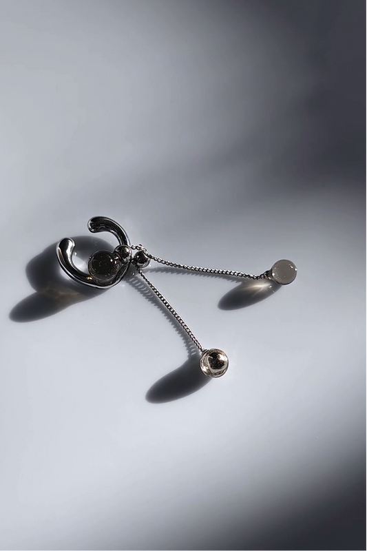 silver ear cuff with trancelucent black orb with detachable drop on flat surface.