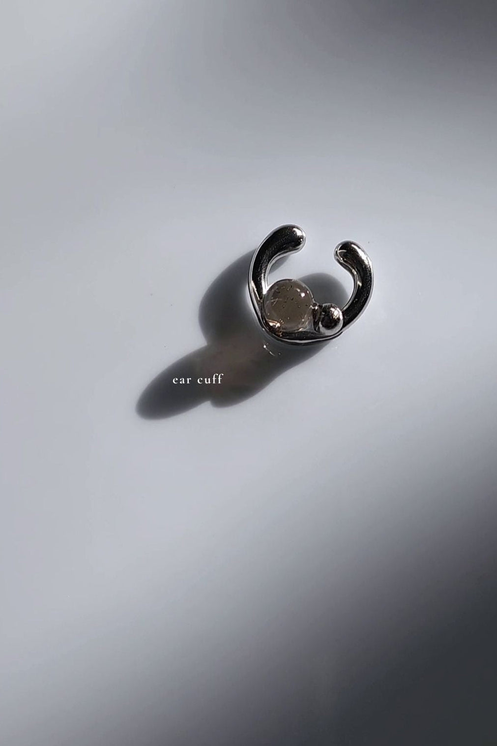 Silver ear cuff with translucent black orb on flat surface.