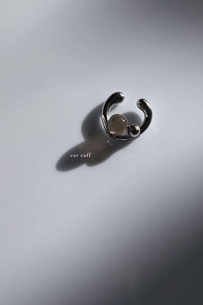Silver ear cuff with translucent black orb on flat surface.