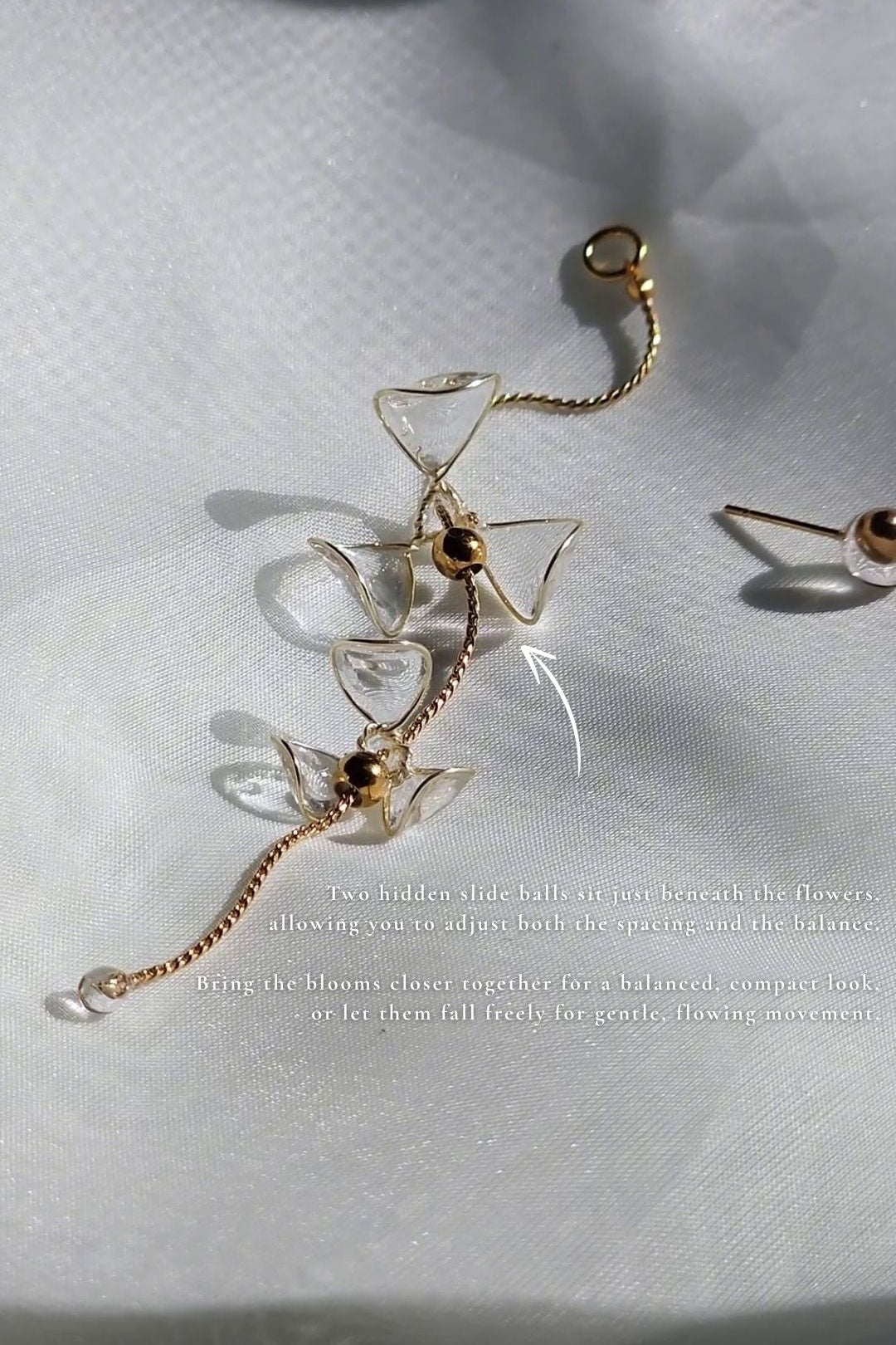 Clear floral drop earring with 2 flowers, MEIKA gold long drop, on a flat surface with detailed explantion for the slide balls.