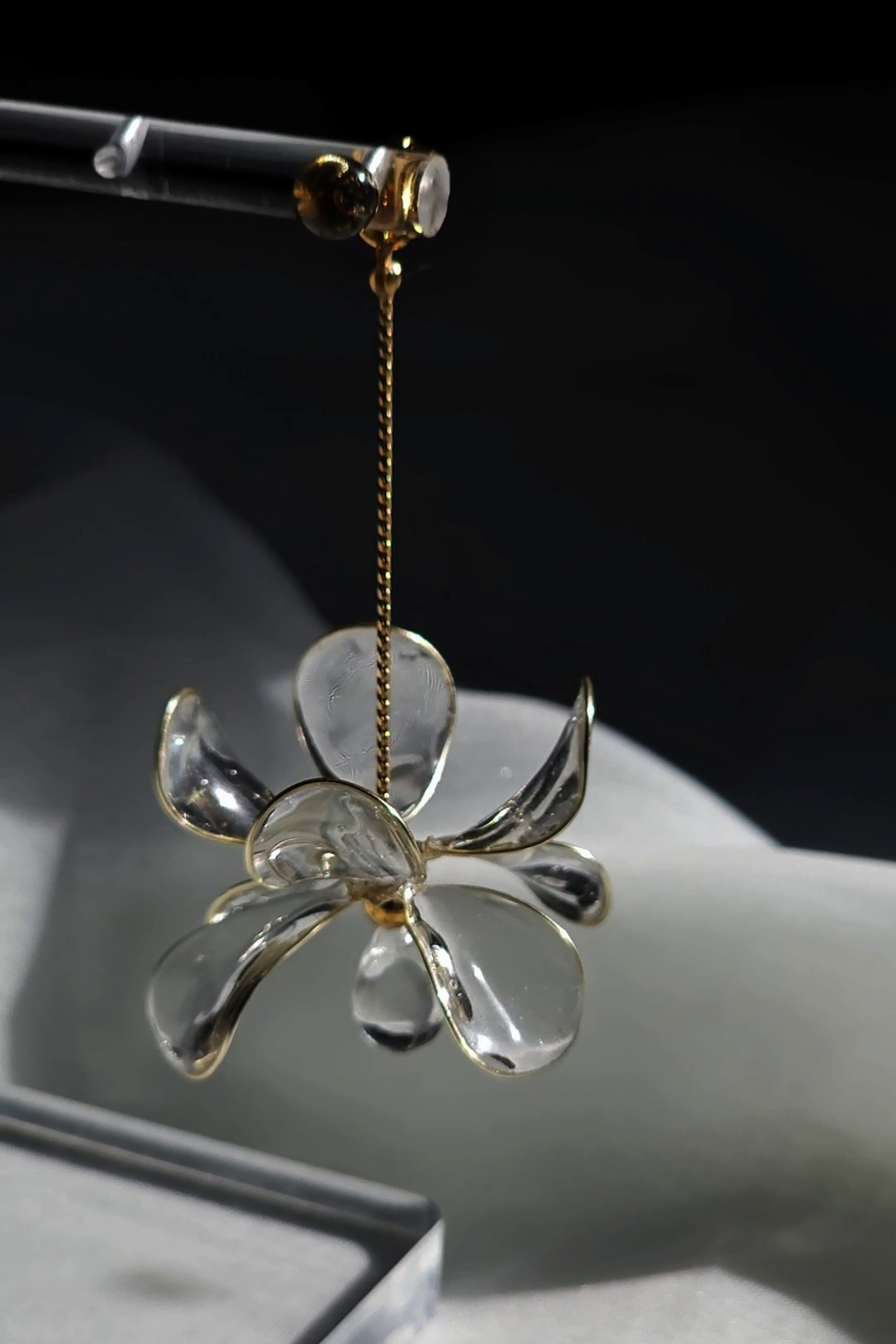 Clear glass flower-shaped drop earring, MEIKA gold short drop with dark background.