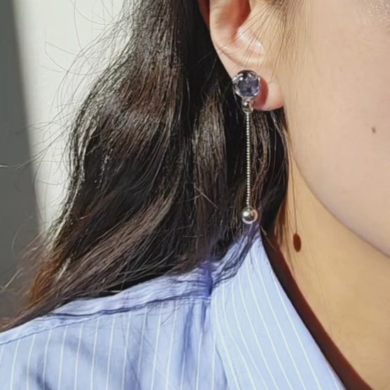 video of a model wearing SORA short drop earring with shimmering chain and hand-blended blue orb that changes color with the light.