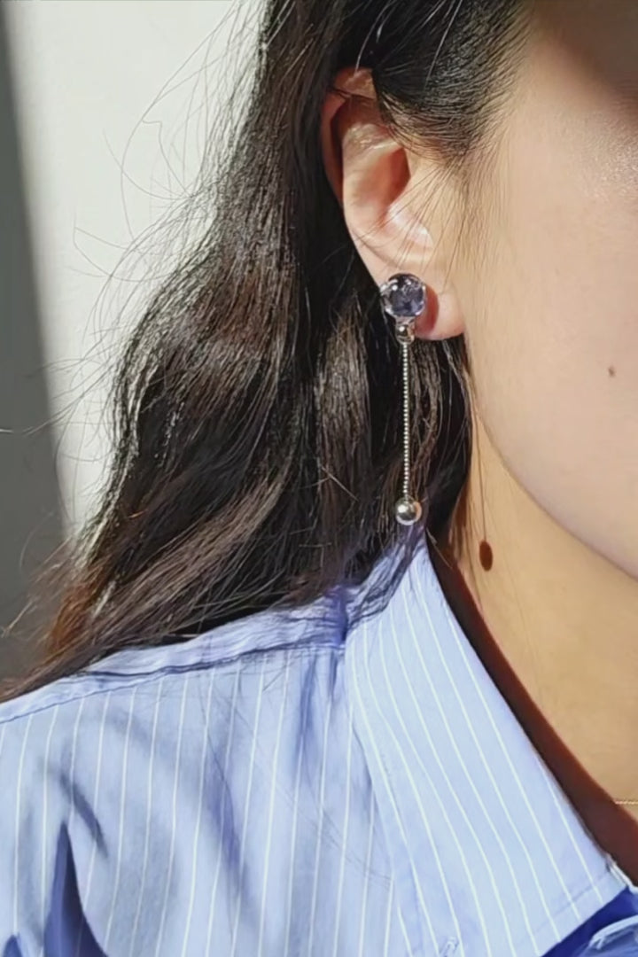 video of a model wearing SORA short drop earring with shimmering chain and hand-blended blue orb that changes color with the light.