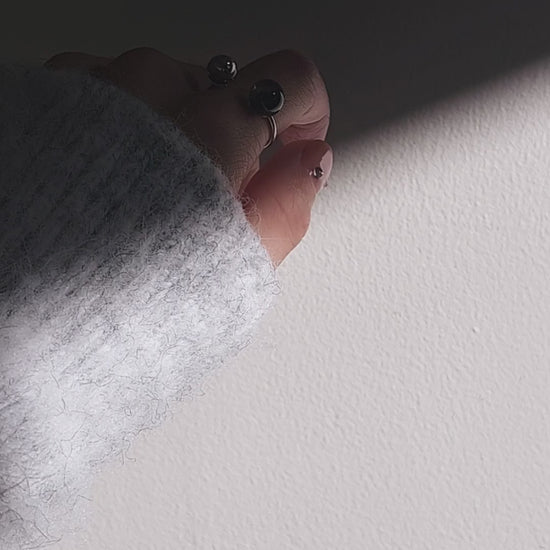 Close-up of a hand wearing double orb ring, KAGE double ring, on index finger and showcasing how the tone changes from translucent black to deep black.