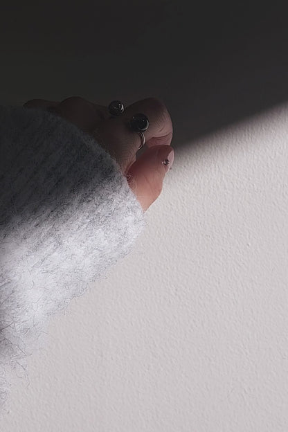 Close-up of a hand wearing double orb ring, KAGE double ring, on index finger and showcasing how the tone changes from translucent black to deep black.