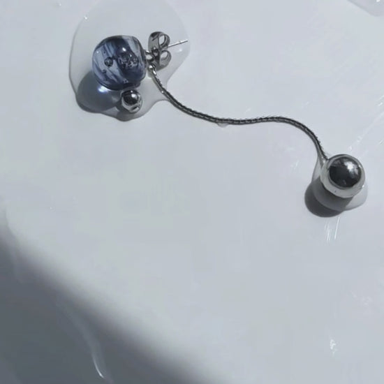 A video of the SORA short drop earring with detachable chain—features a hand-molded blue orb that shifts in tone like the sky, shown laid on neutral surface.
