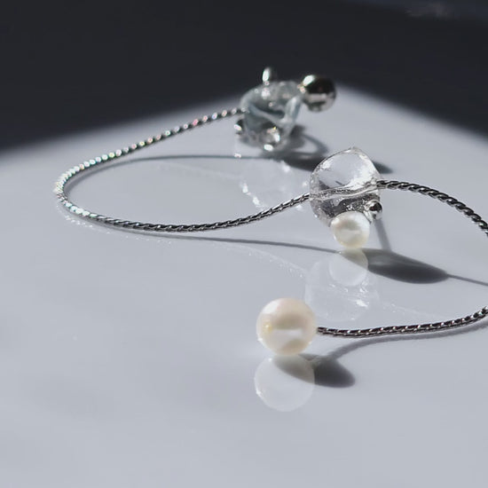 Close-up video of NAMI multiway ear cuff and stud connected by chain with freshwater pearls, featuring hand-blended silvery-blue and gray tones inspired by ocean waves.