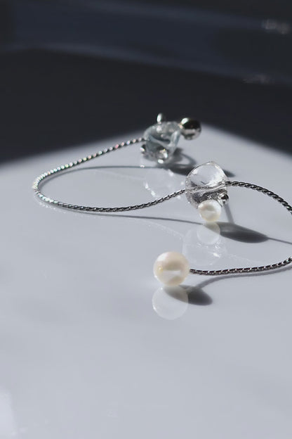 Close-up video of NAMI multiway ear cuff and stud connected by chain with freshwater pearls, featuring hand-blended silvery-blue and gray tones inspired by ocean waves.