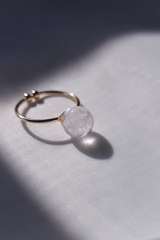 Gold ring with a melting ice-like orb as a centrepiece on a light gray background