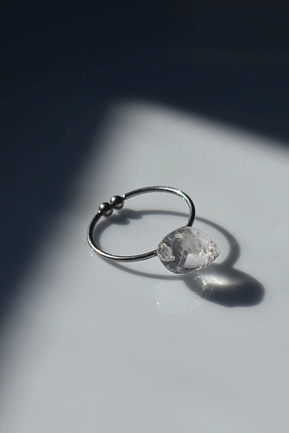 REI ring laid flat, showing its delicate metal band and hand-molded centerpiece resembling melting ice.