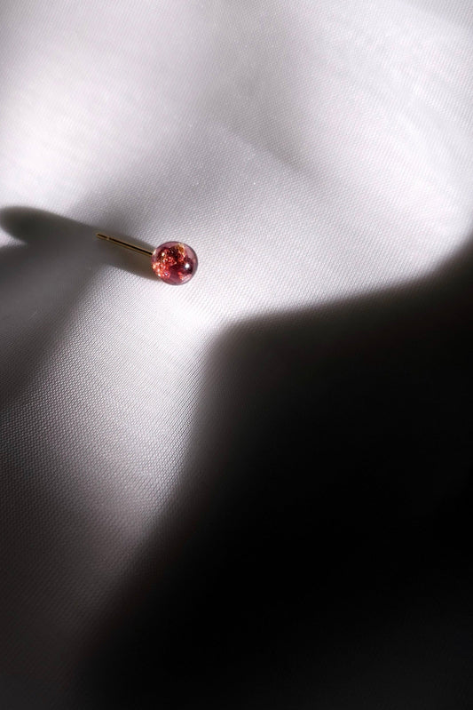 A single dark cherry colored stud earring, SAKURAMBO micro stud on a flat surface