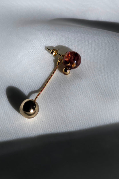 A multiway short orb drop in dark cherry with a detachable gold orb, SAKURAMBO short drop, on a flat surface. 