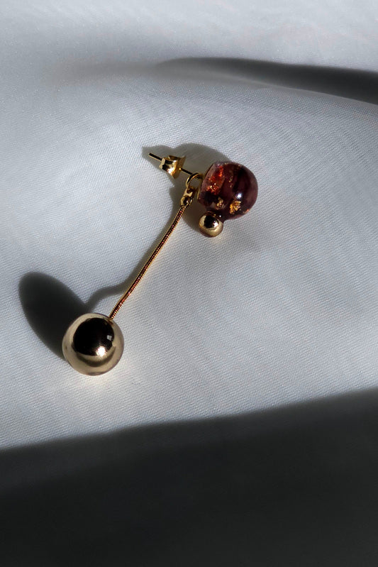 A multiway short orb drop in dark cherry with a detachable gold orb, SAKURAMBO short drop, on a flat surface. 