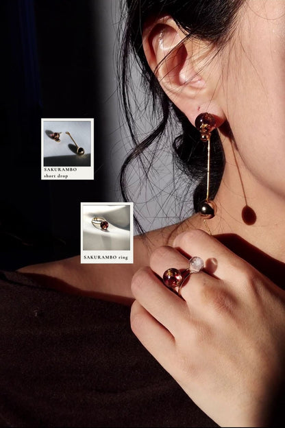 Model wearing 10mm orb ring in dark cherry in the middle finger with orb short drop in dark cherry, SAKURAMBO short drop.