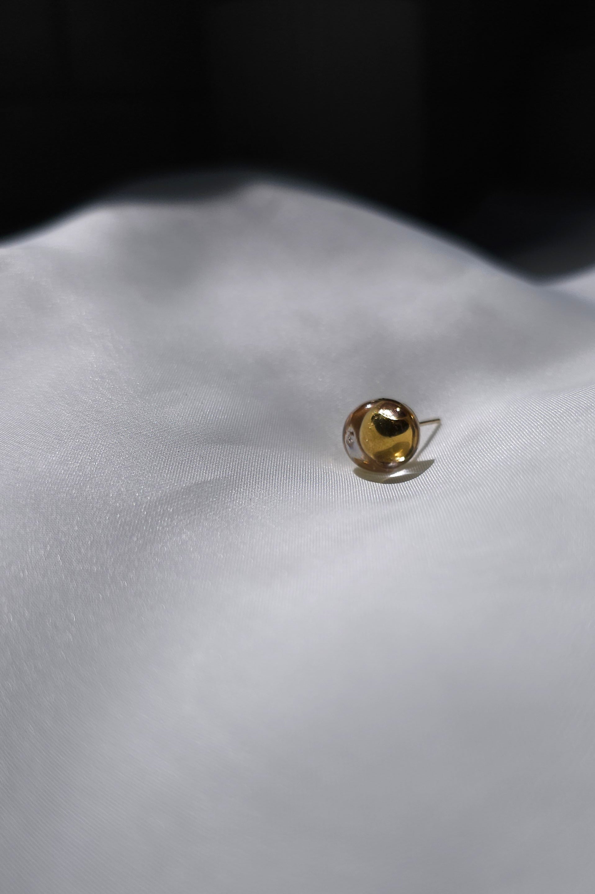 TSUYU gold stud earring, inspired by shimmering beads of dew, with warm golden reflections that change in the light.